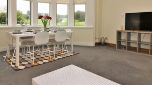 Een eetgedeelte met een tafel voor vier personen, een vaas met bloemen en uitzicht op een groen landschap door grote ramen.