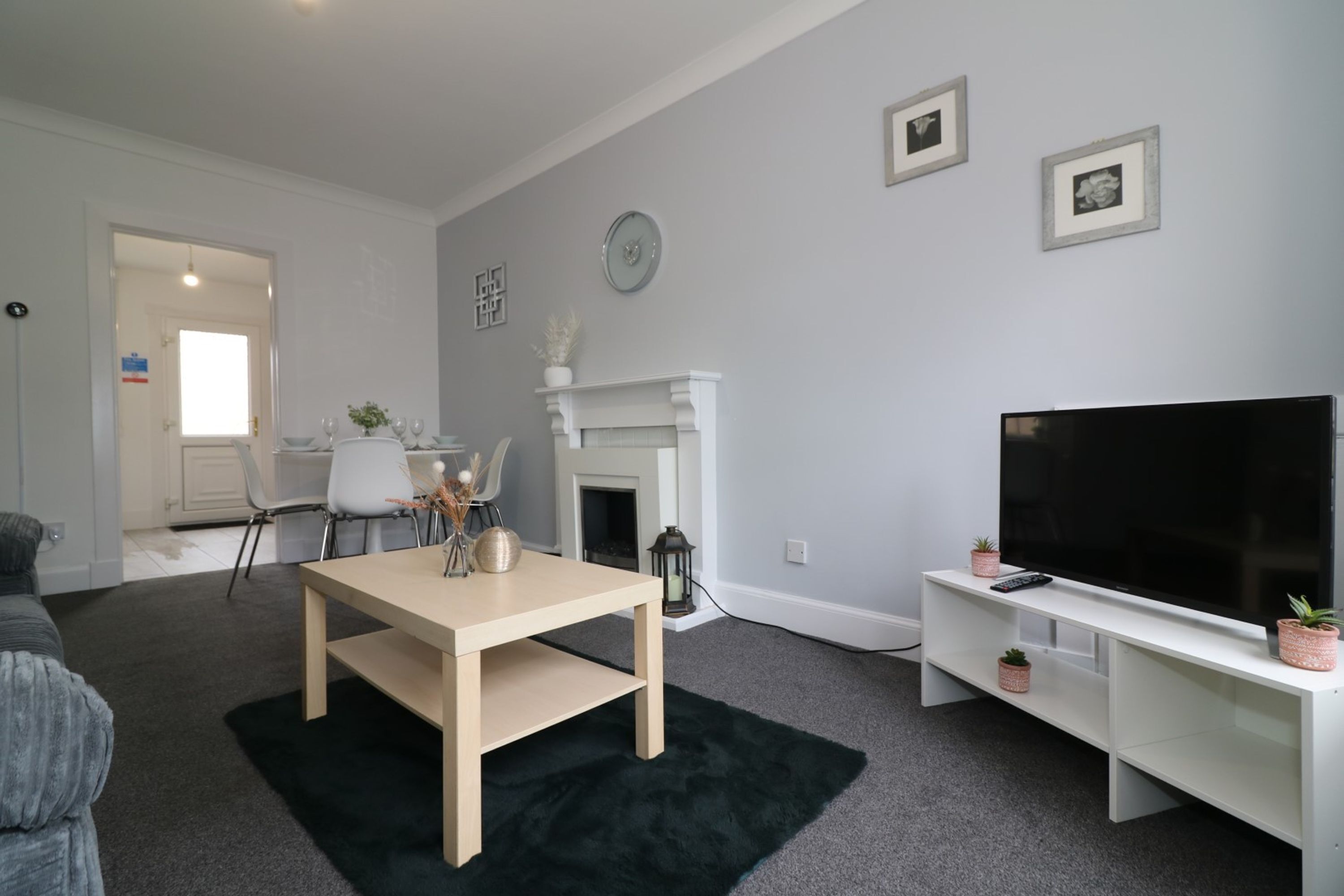 Una sala de estar moderna con chimenea, un televisor sobre un mueble blanco, una mesa de comedor y un sofá.
