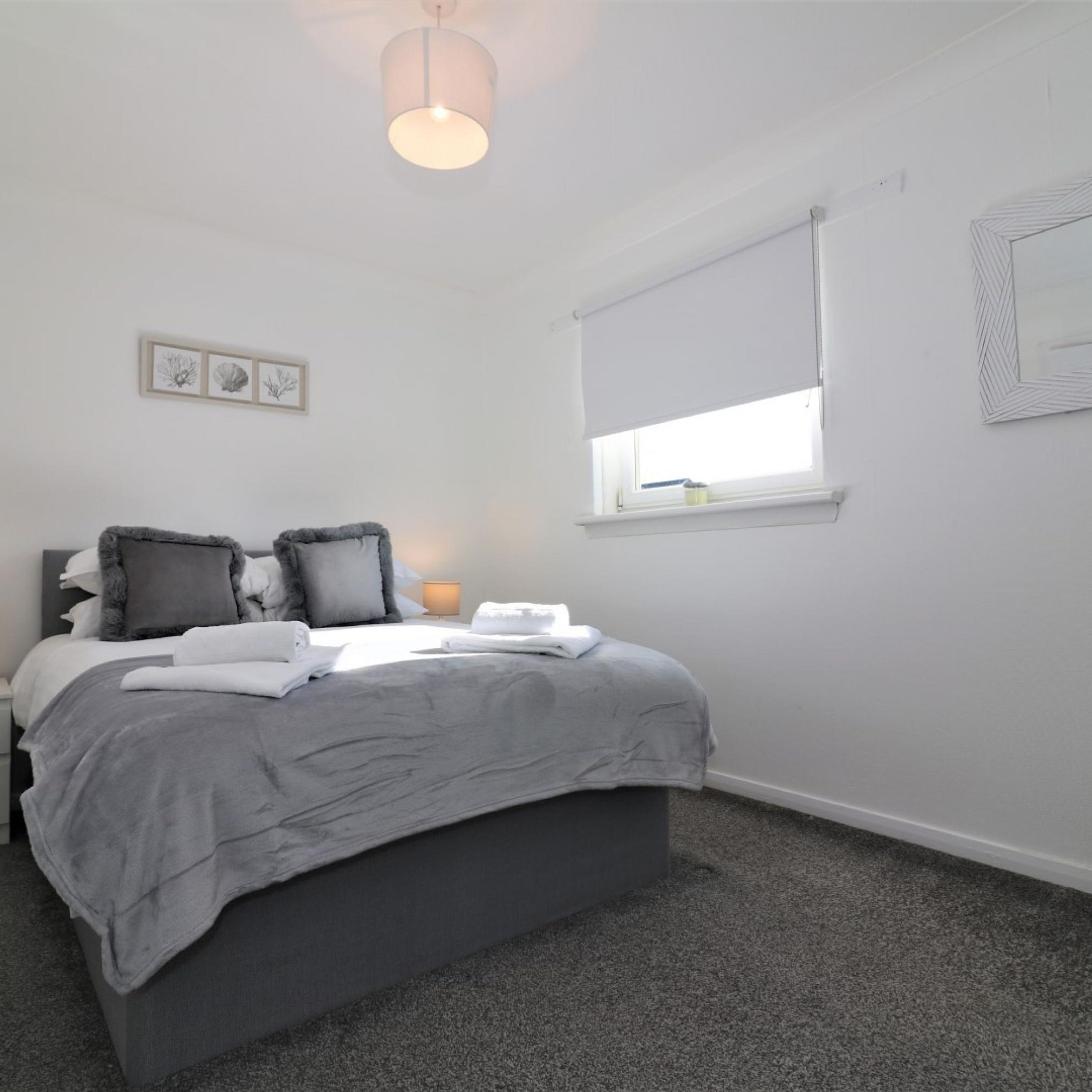 A bedroom with a bed, a bedside lamp, a window with a blind, and a ceiling light fixture.