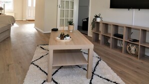 Una sala de estar con una mesa de centro de madera, un televisor montado en la pared y una estantería.