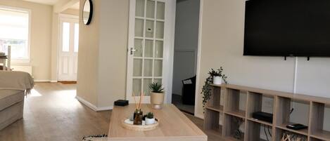 A living room with a wooden coffee table, a TV mounted on the wall, and a bookshelf.