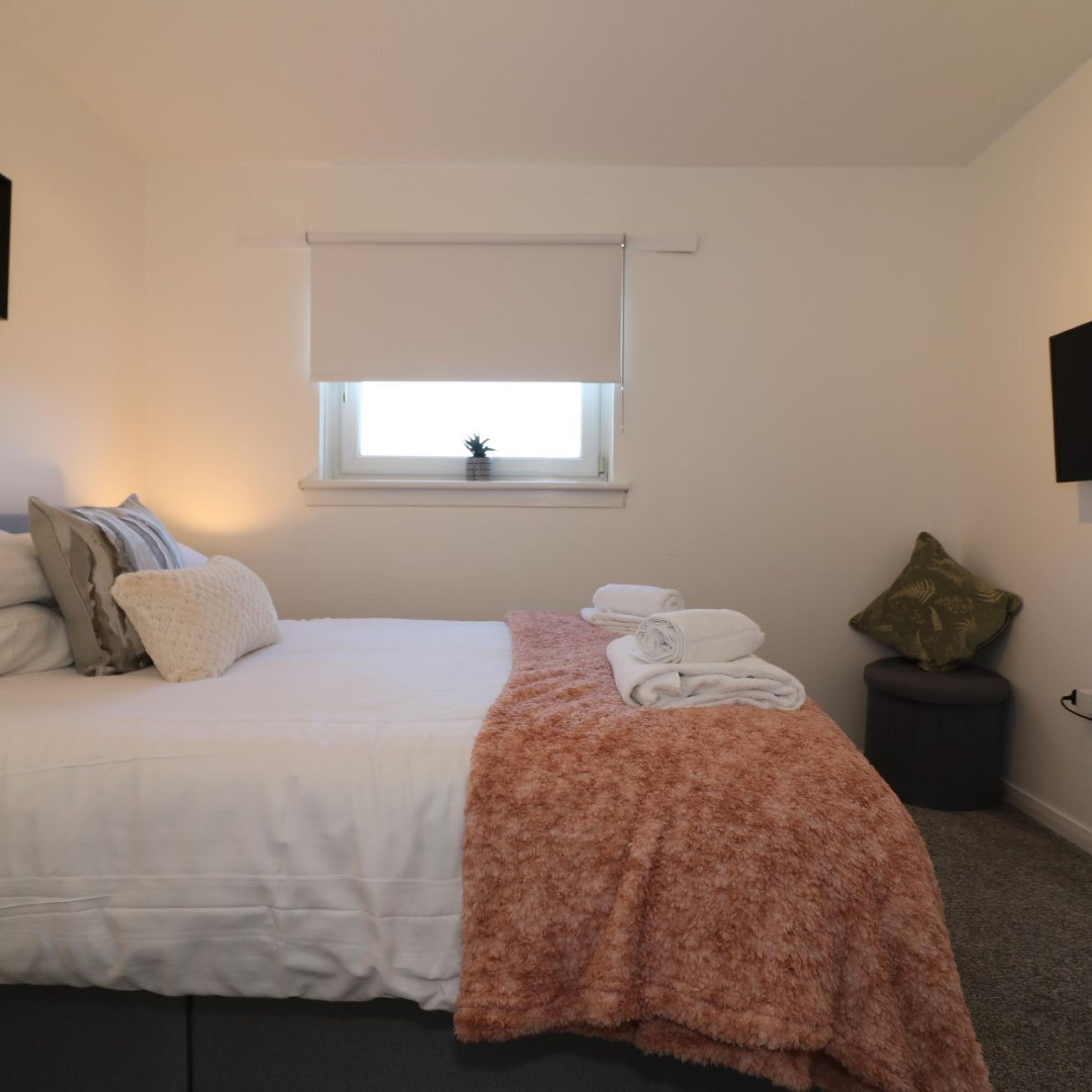 Un dormitorio con cama, ventana con vistas, planta pequeña y televisor de pared.