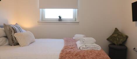 Ein Schlafzimmer mit Bett, Fenster mit Blick, einer kleinen Pflanze und einem an der Wand befestigten Fernseher.