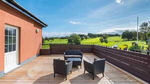 A wooden deck with outdoor furniture, a view of a golf course, and a building with a red exterior. - Greenlees Clubhouse 2 bed - Cambuslang (Glasgow)