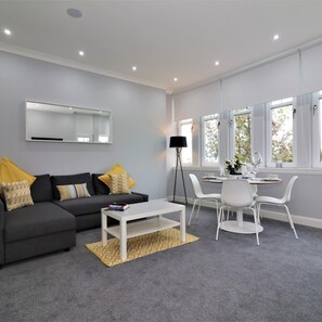 Un salon moderne avec un canapé gris, une table basse blanche et un coin repas comprenant une table et des chaises blanches.