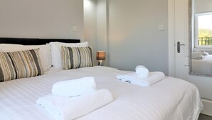 A neatly made bed with white linens and two rolled towels, a bedside lamp, and a mirror on the wall. - Greenlees Clubhouse 2 bed - Cambuslang (Glasgow)
