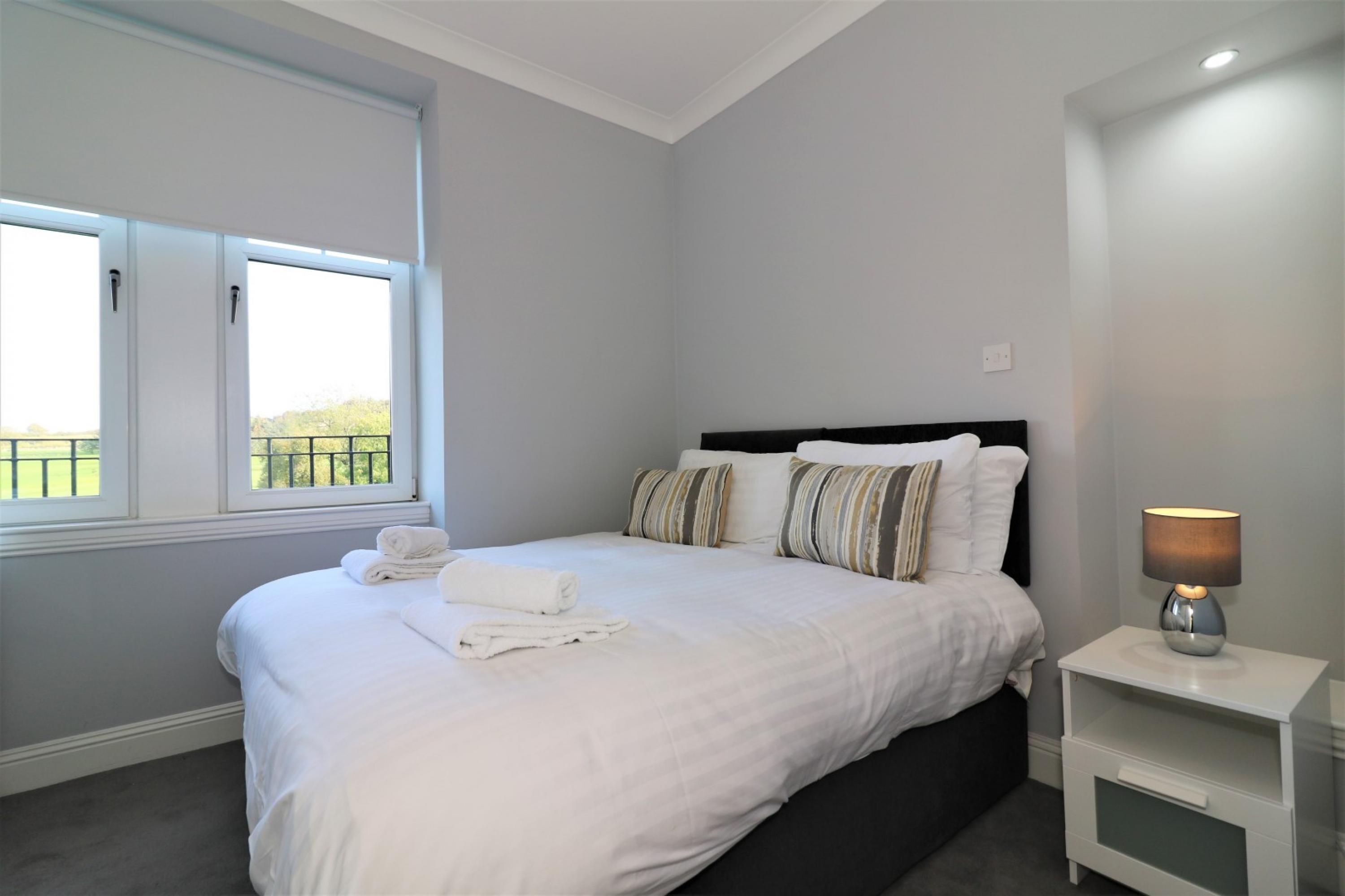 A bedroom with a bed, a nightstand, a lamp, and a window with a view of greenery.