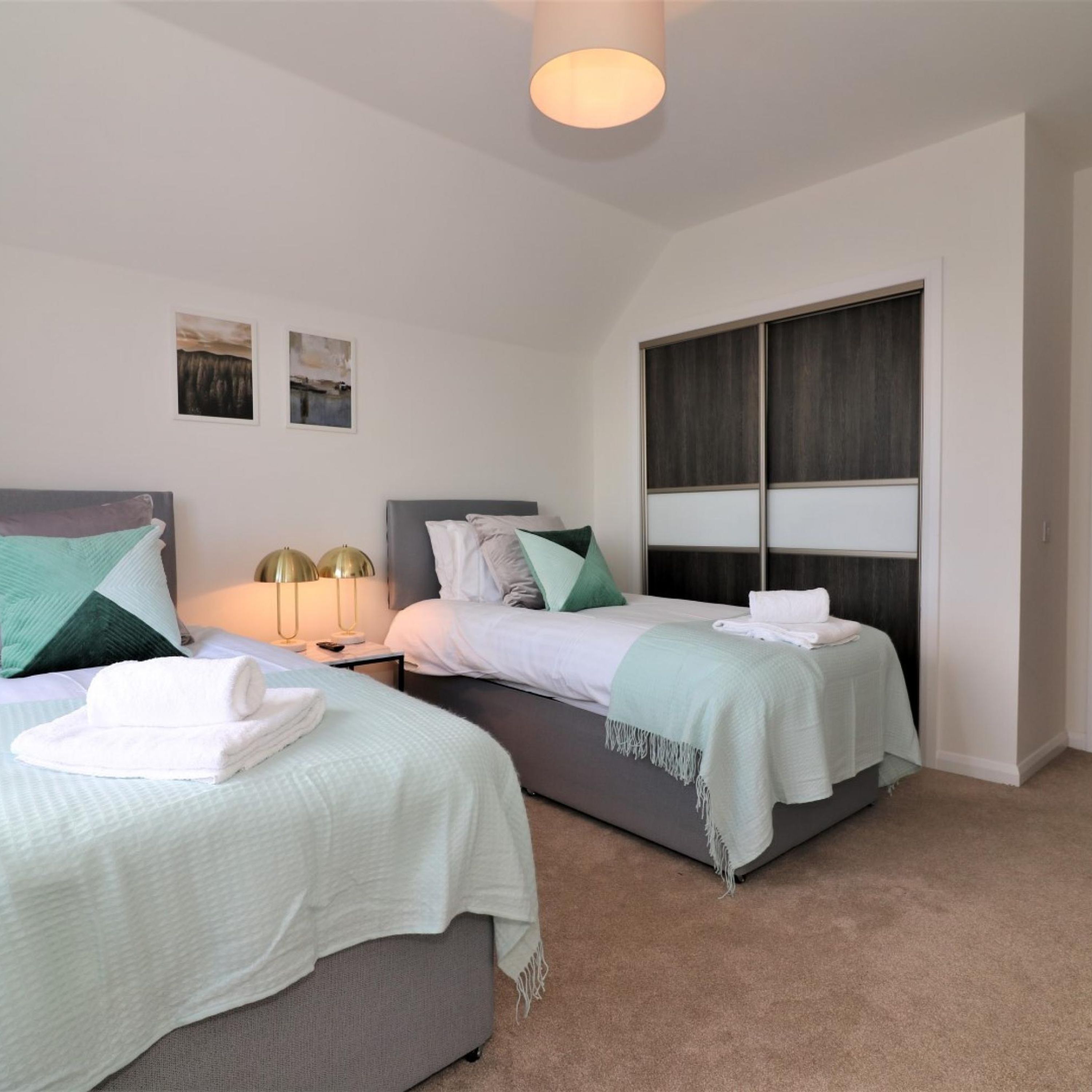 A modern bedroom with two beds, a large window, and a ceiling light.