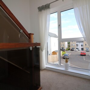 A room with a large window, a wooden staircase, and a view of a residential street. - Macneish House - East Kilbride (Glasgow)