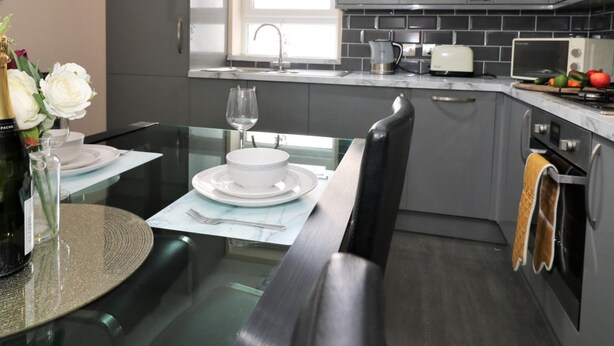 Una cucina moderna con mobili grigi, un piano di lavoro nero e un'area pranzo con tavolo e sedie in vetro.
