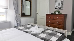 Una camera da letto con un letto, una cassettiera, uno specchio, un termosifone, una porta e una finestra con tende.