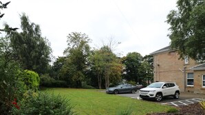Un espace de stationnement avec deux voitures, une pelouse et un bâtiment à la façade en briques.