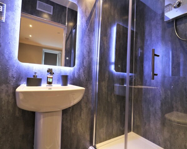 A modern bathroom with a pedestal sink, a large mirror, and a glass-enclosed shower area.