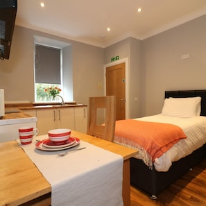 A room with a bed, a table with a white tablecloth, and a window with flowers. - Linden Cottage Room 2 - Airdrie (Airdrie)