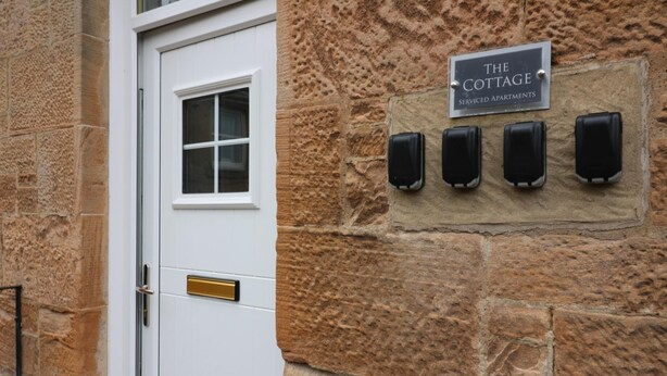 Un mur de pierre avec une porte et une enseigne indiquant : « The Cottage Serviced Apartments ».