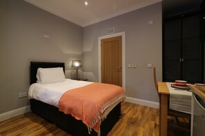 A bedroom with a bed, a nightstand, a lamp, a wooden door, and a small table with a bowl and plates. - Linden Cottage Room 2 - Airdrie (Airdrie)