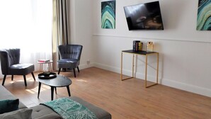 Un salon moderne avec un canapé, deux fauteuils, une table basse et un téléviseur fixé au mur.