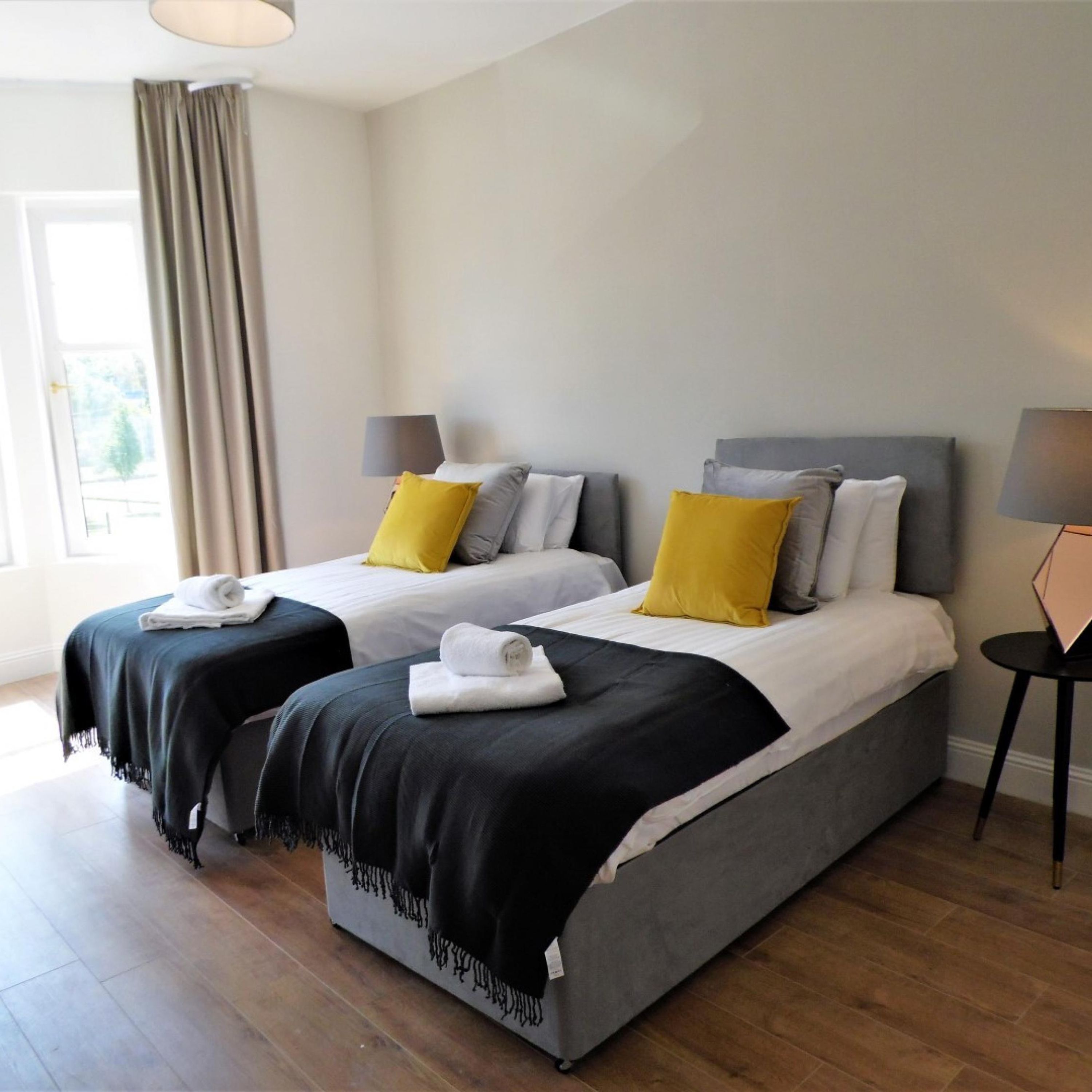 A double bed with a grey headboard, two pillows, and a black throw blanket.