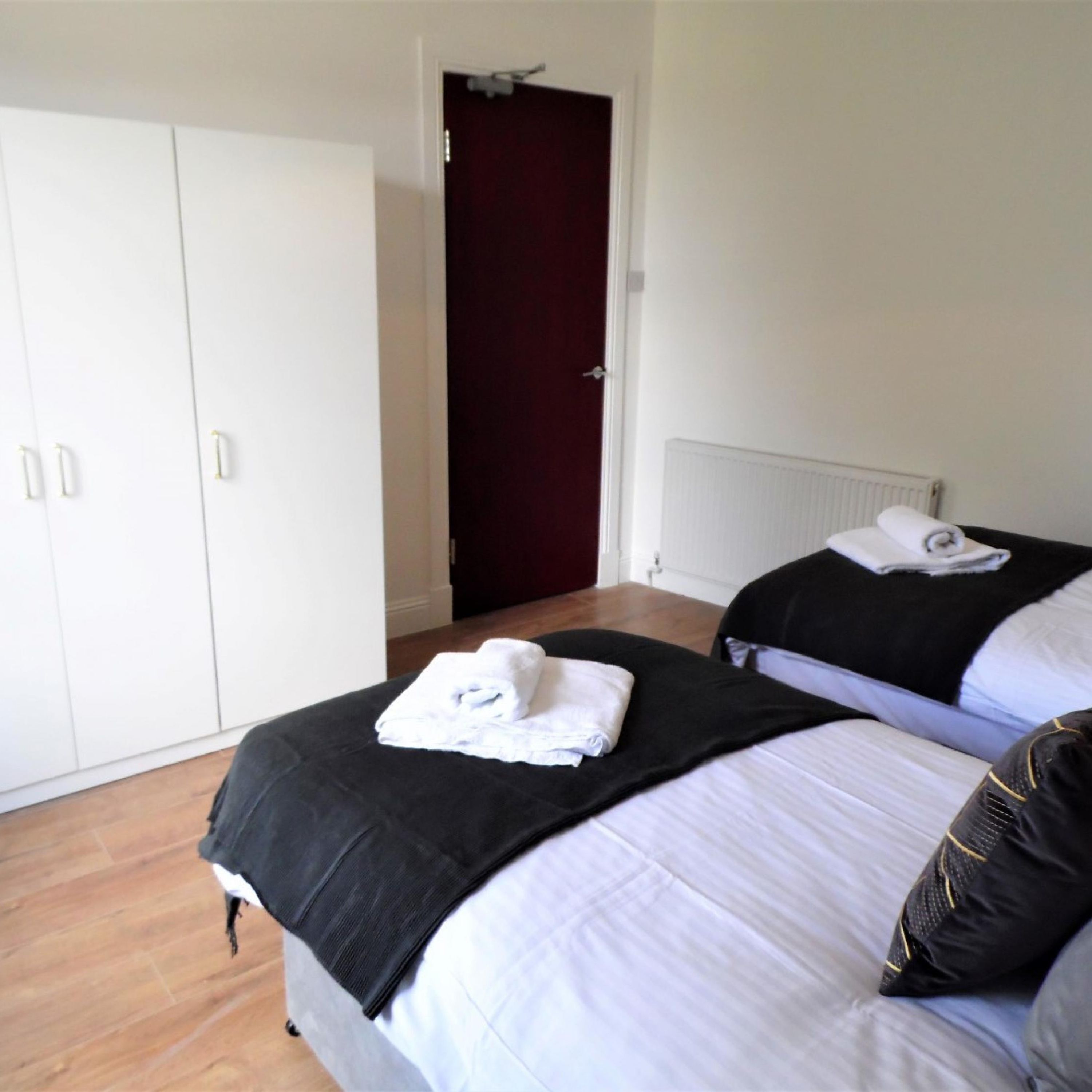 A hotel room with two beds, a wardrobe, and a door leading to another room.