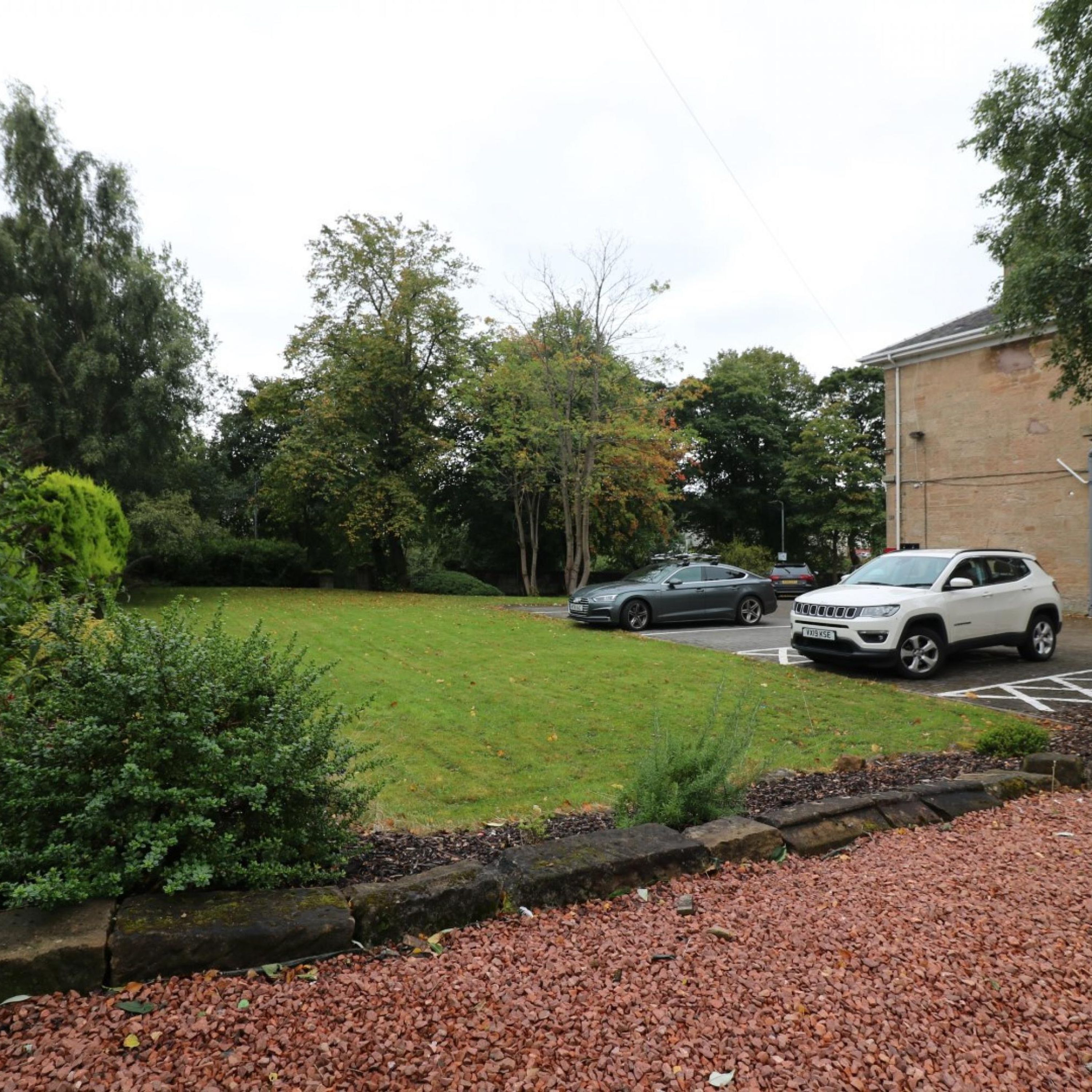 A parking area with two cars, a grassy lawn, and trees.