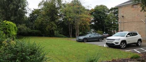 A parking area with two cars, a grassy lawn, and trees.