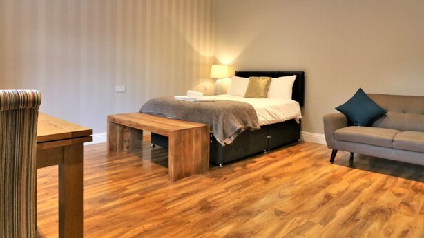 A modern bedroom with a bed, a sofa, a wooden bench, and a table. - Linden Cottage Room 1 - Airdrie (Airdrie)