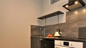 A modern kitchen with a dishwasher, oven, and a kettle on the countertop. - Linden Cottage Room 1 - Airdrie (Airdrie)