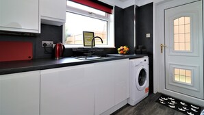 Eine kompakte Küche mit weißen Schränken, einer roten Arbeitsplatte, einem Fenster und einer Waschmaschine.