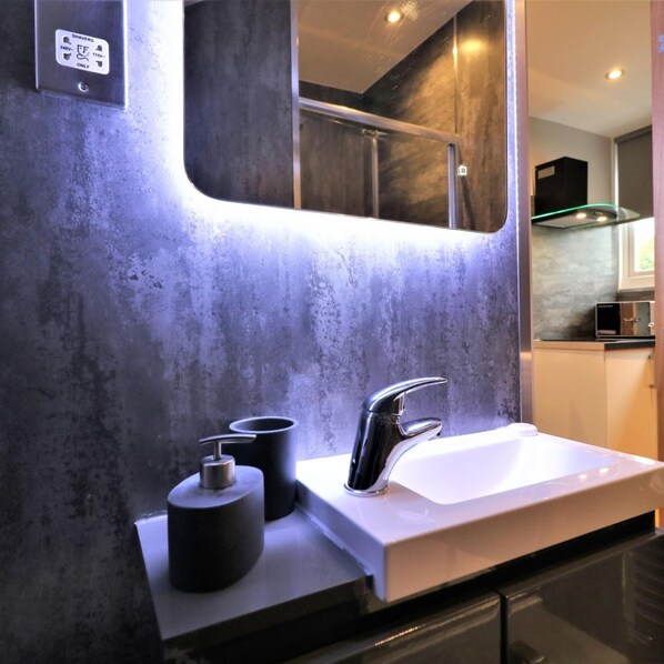 A modern bathroom with a white sink, a black faucet, and a mirror above it. There are two black soap dispensers on the counter.