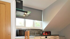 A compact kitchen with a microwave, oven, and a small refrigerator. There is a window above the sink, and a dining table with chairs. - Linden Cottage Room 4 - Airdrie (Airdrie)