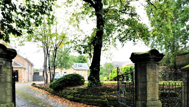 A paved pathway with scattered leaves, flanked by stone pillars and a wrought iron gate. - Linden Cottage Room 4 - Airdrie (Airdrie)