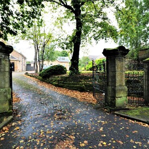 A paved pathway with scattered leaves, flanked by stone pillars and a wrought iron gate. - Linden Cottage Room 4 - Airdrie (Airdrie)