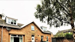 A two-story house with a brick exterior, a front door, and a small front yard covered with red leaves. - Linden Cottage Room 4 - Airdrie (Airdrie)