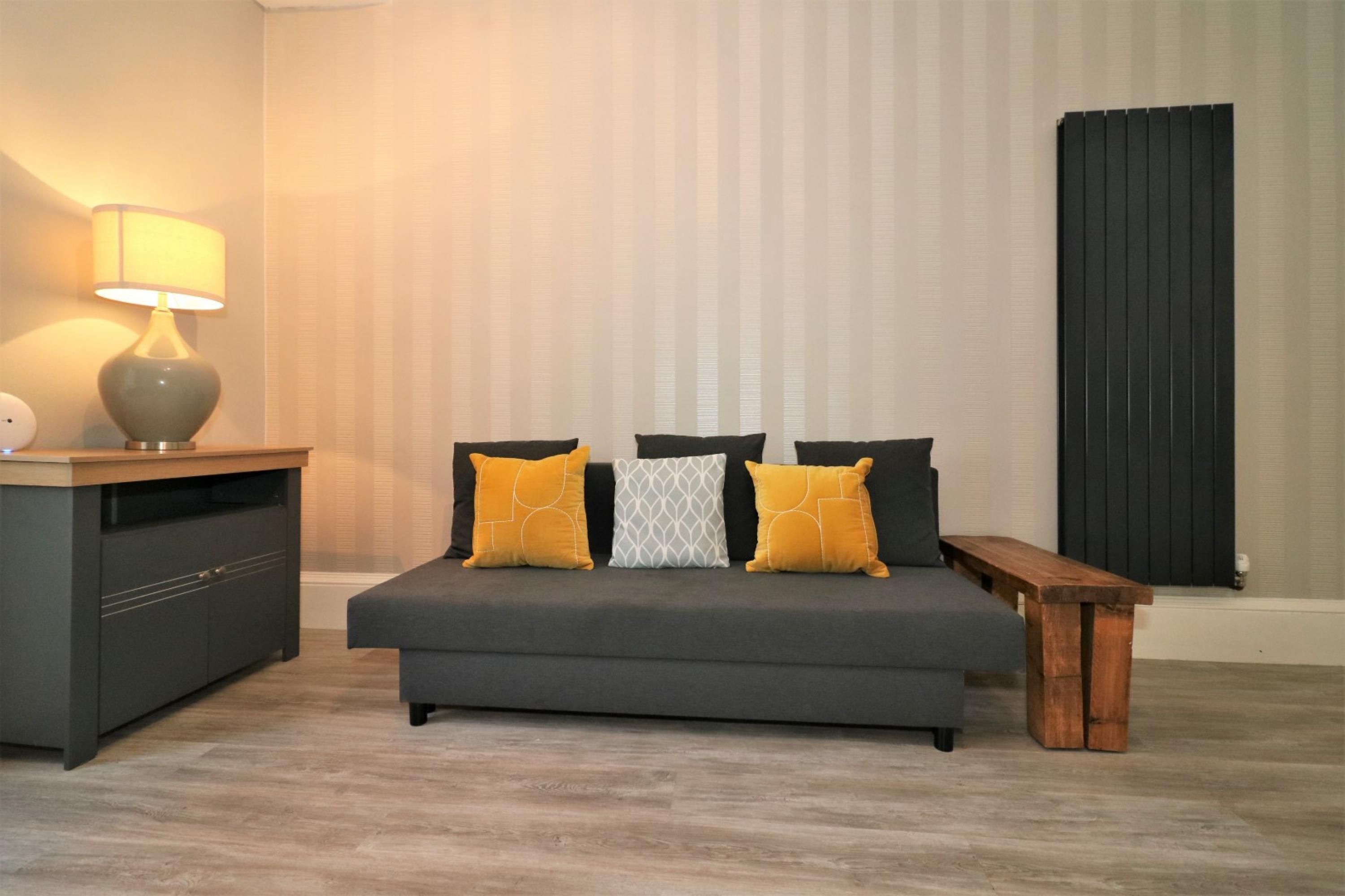A modern bedroom with a grey sofa, wooden bench, and a bedside table with a lamp.