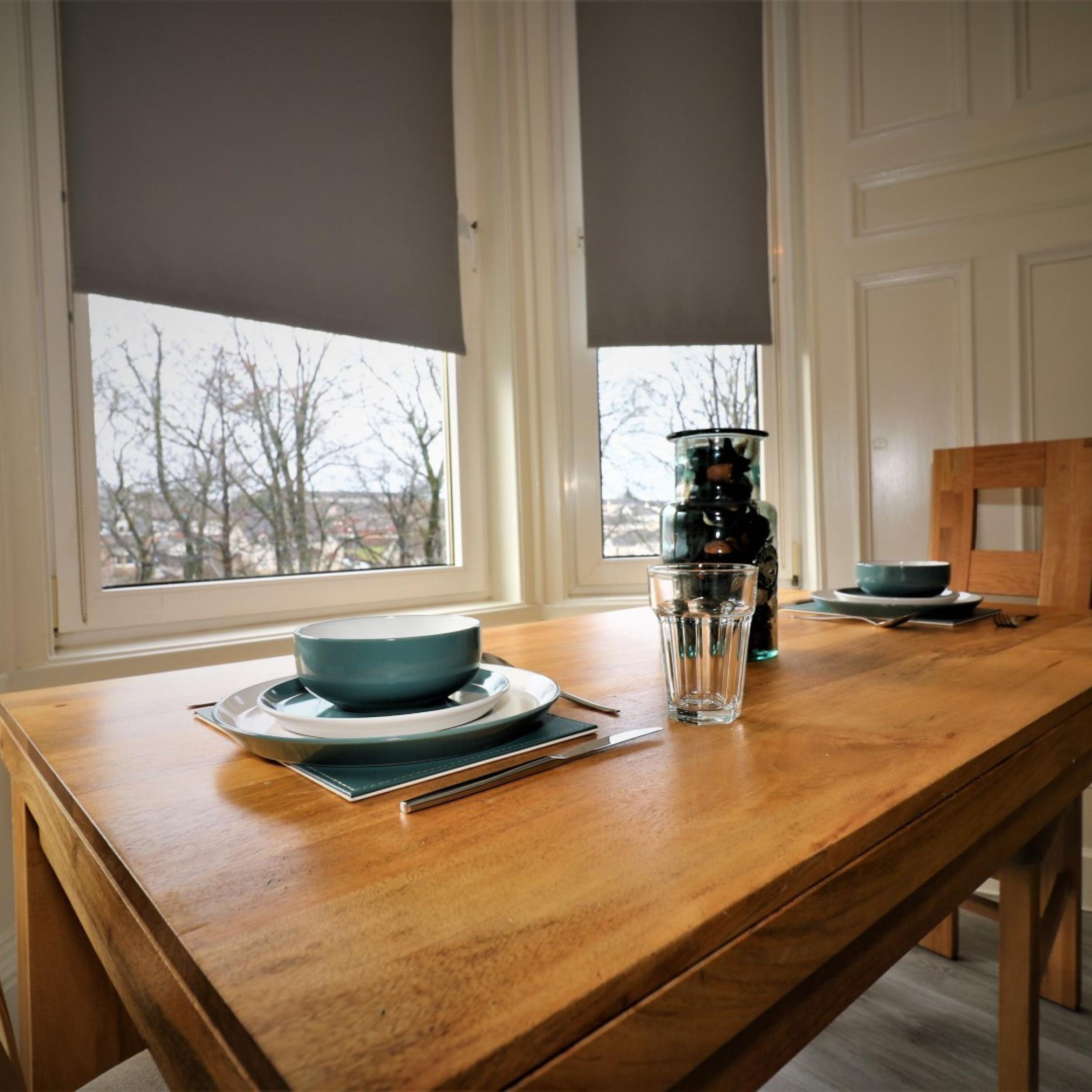 A wooden dining table with a blue bowl and a glass on it, a bottle, and a bowl on a plate.