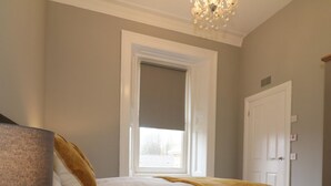 A bedroom with a bed, a nightstand, a lamp, a window, and a door. - Linden House - Flat 3 - Airdrie (Airdrie)