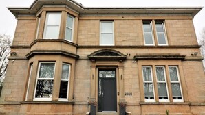 A two-story stone building with a black front door, large windows, and a small porch with steps leading up to the entrance. - Linden House - Flat 3 - Airdrie (Airdrie)