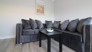 A modern living room with a dark grey sectional sofa, a black coffee table, and a framed artwork on the wall. - Sunnyside House - Holytown (Motherwell)