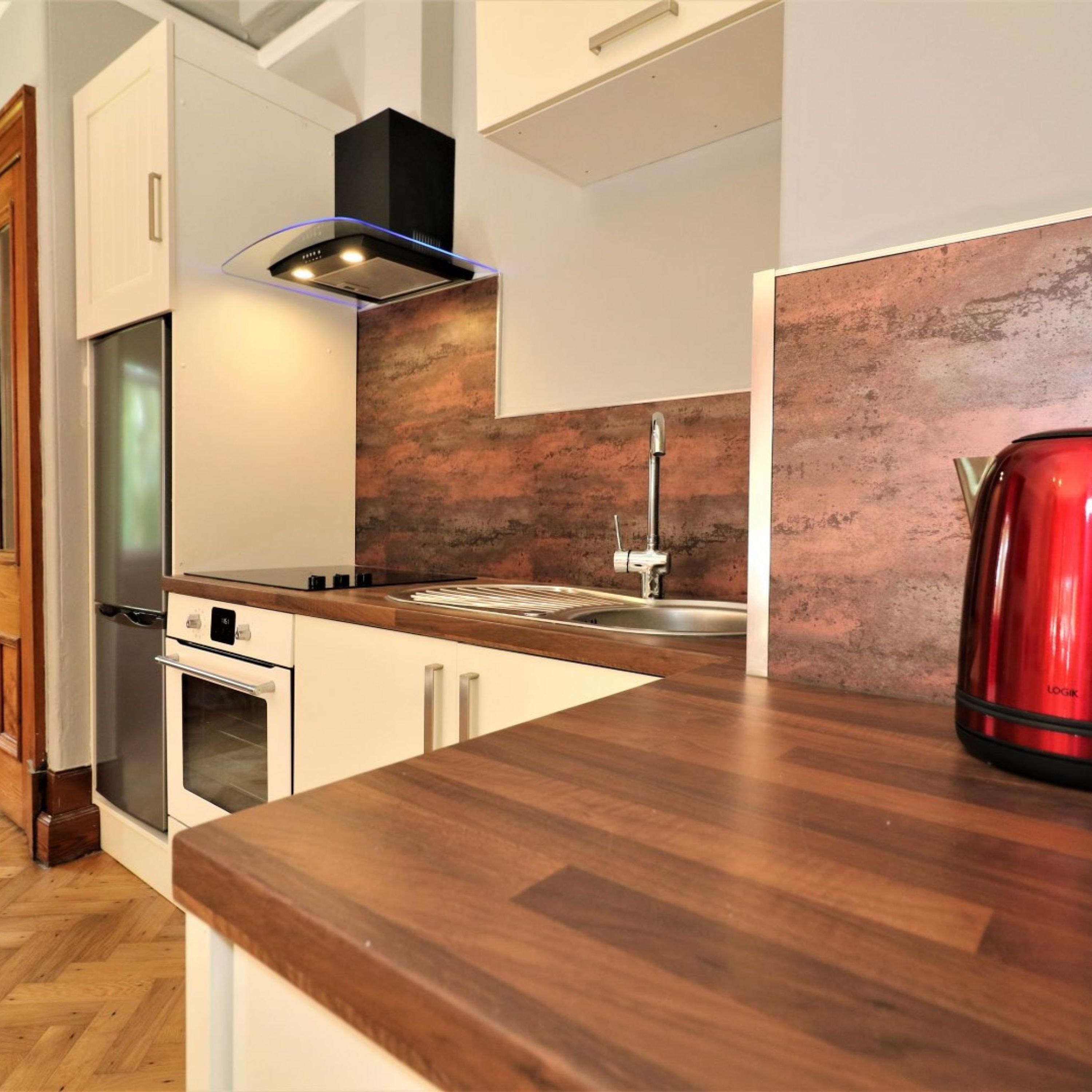 A modern kitchen with a wooden countertop, stainless steel appliances, and a red kettle.