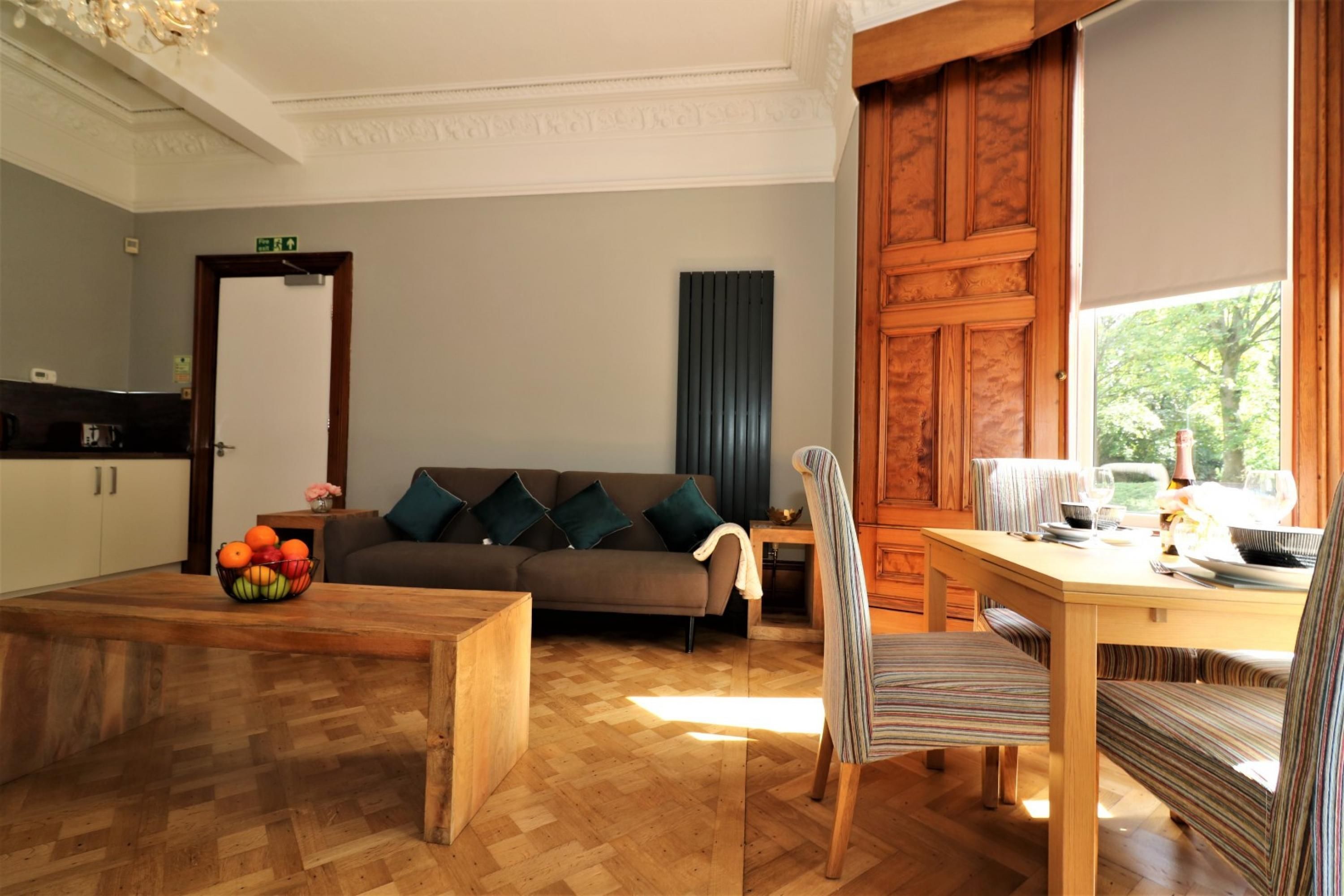 Un salon avec une table basse en bois, un canapé avec des coussins, un fauteuil à rayures et une table à manger dressée pour deux personnes.