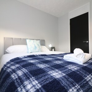 Un lit bien fait, recouvert d’une couverture à carreaux bleus et blancs, avec un oreiller blanc et une serviette blanche pliée posée sur le lit.