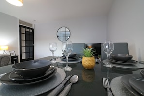 Une table à manger dressée avec des assiettes, des bols, des couverts et des verres à vin, agrémentée d’un ananas en guise de centre de table et d’un miroir accroché au mur.