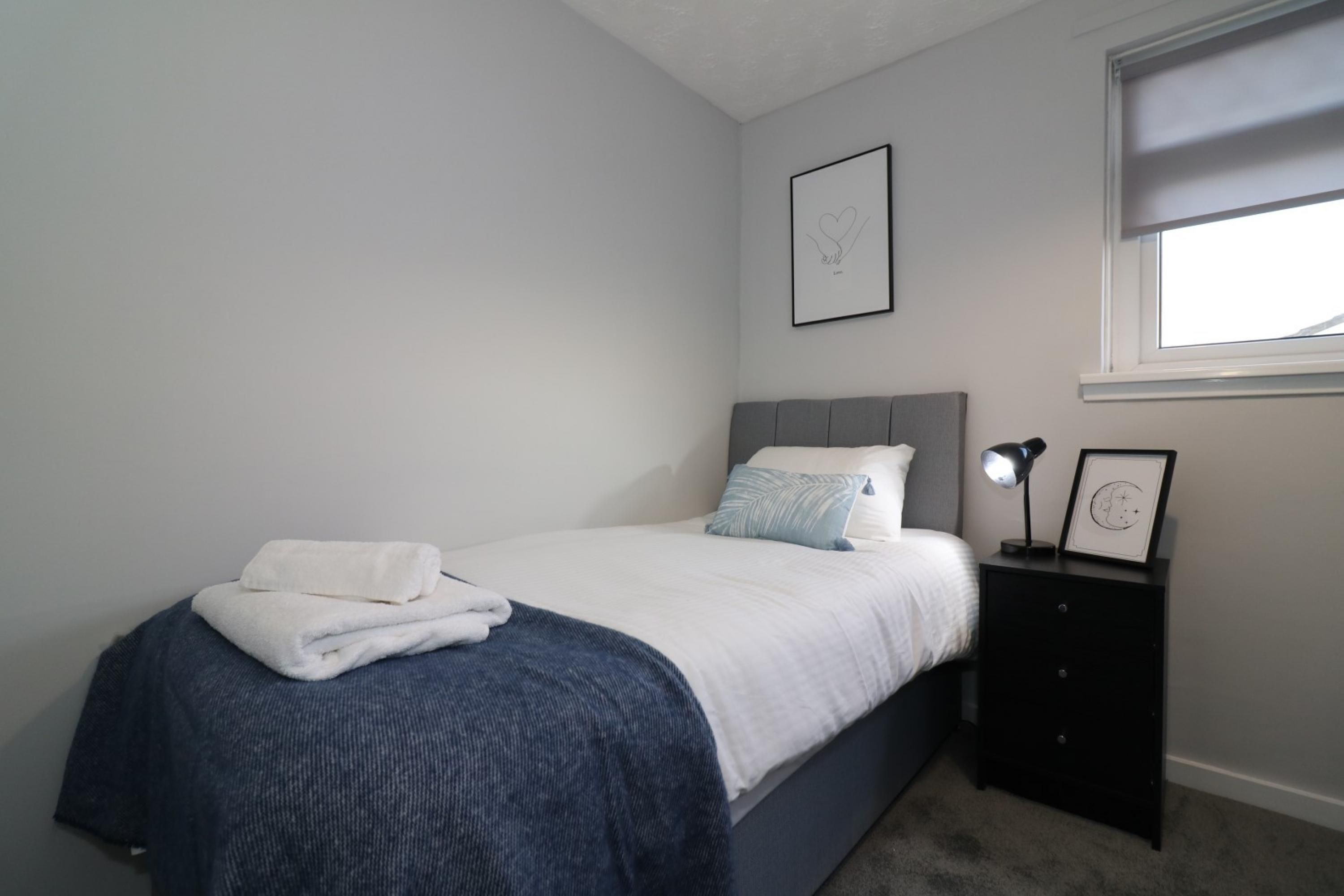 A bedroom with a bed, a nightstand, a window, and two framed pictures on the wall.
