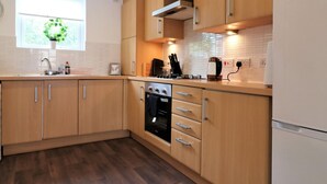 A modern kitchen with wooden cabinets, a built-in oven, and a refrigerator. - Belvidere House - Parkhead (Glasgow)