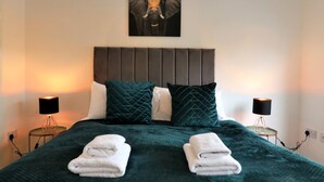 A neatly made bed with a dark green blanket, two white towels, and a headboard with a picture of an elephant. - Belvidere House - Parkhead (Glasgow)