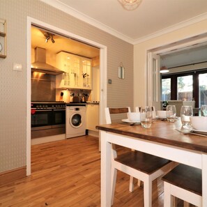 A compact kitchen with modern appliances, a dining area with a wooden table and chairs, and a view through an open door. - Shield House - Govan (Glasgow)