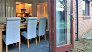 A dining area with a wooden table and four grey chairs, a sliding glass door leading outside, and a visible outdoor area with a wooden deck. - Shield House - Govan (Glasgow)