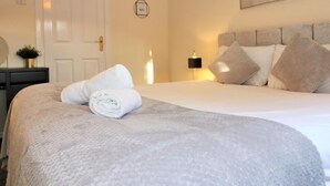 A neatly made bed with a white duvet and rolled towels, a bedside table with a lamp, and a wall-mounted artwork. - Shield House - Govan (Glasgow)