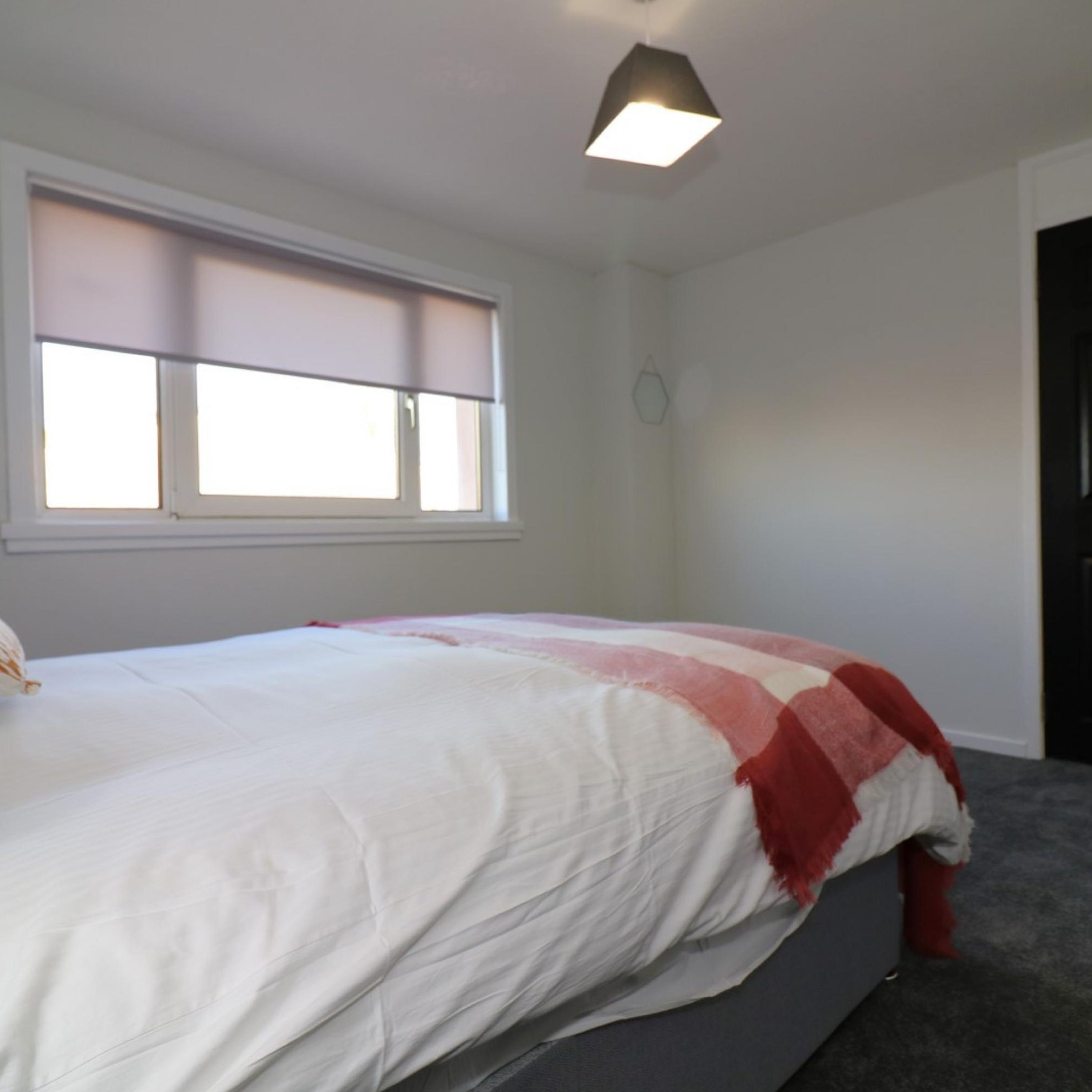 Ein Schlafzimmer mit einem Bett, einem Fenster mit Jalousien und einer Deckenleuchte.
