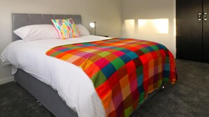 Une chambre d’hôtel moderne avec un lit soigneusement fait, une courtepointe aux couleurs vives, une tête de lit grise et une armoire noire.